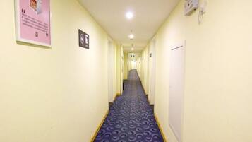 Um corredor de hotel com carpete estampado, uma placa à esquerda e uma porta à direita.