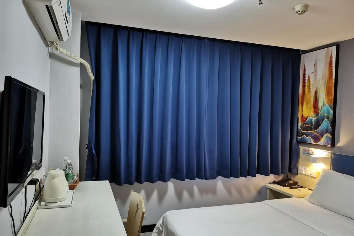 A hotel room with a bed, a desk, a chair, a television, and a painting on the wall.