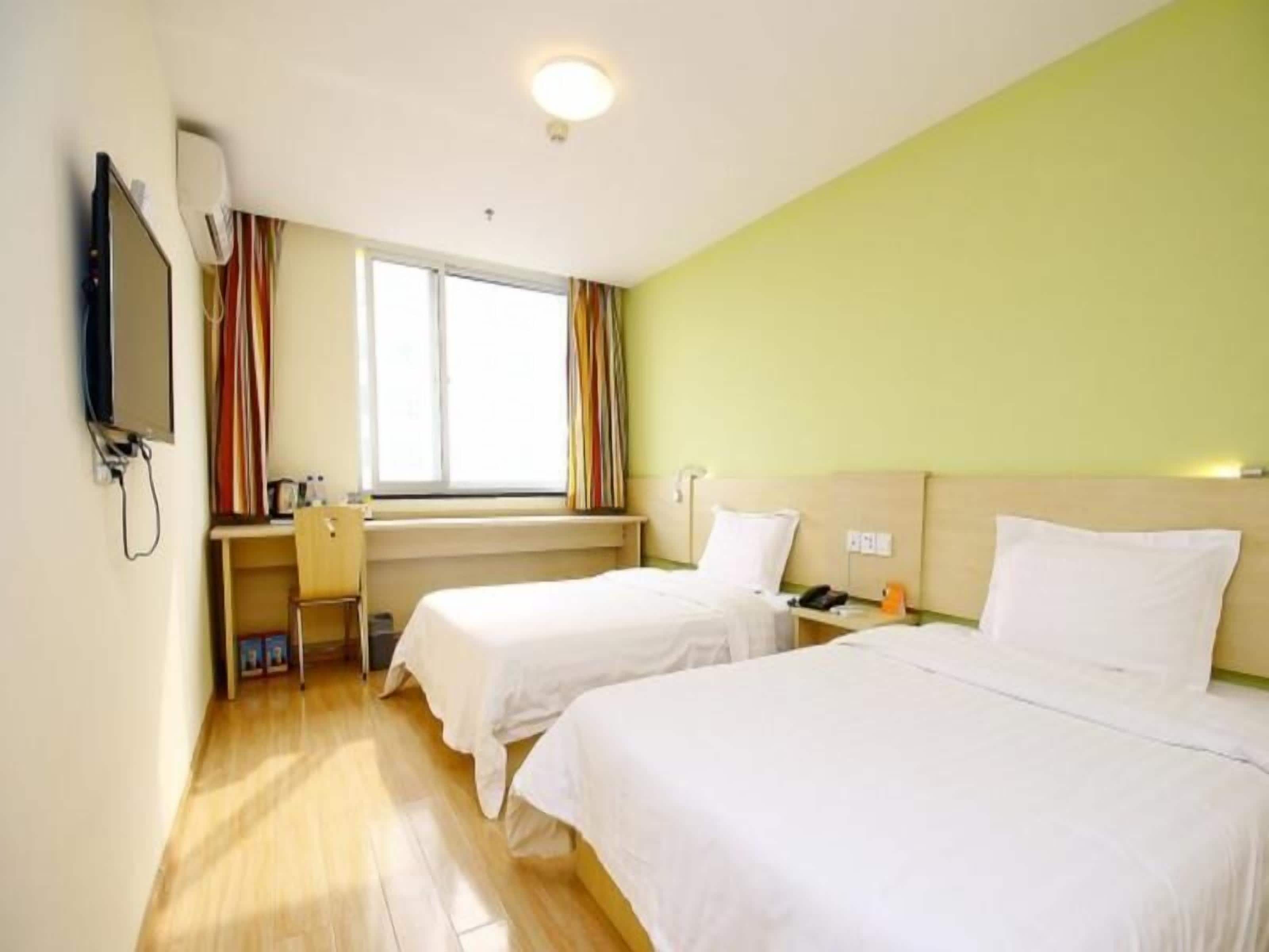 A hotel room with two beds, a desk with a chair, a TV, and a window with curtains.