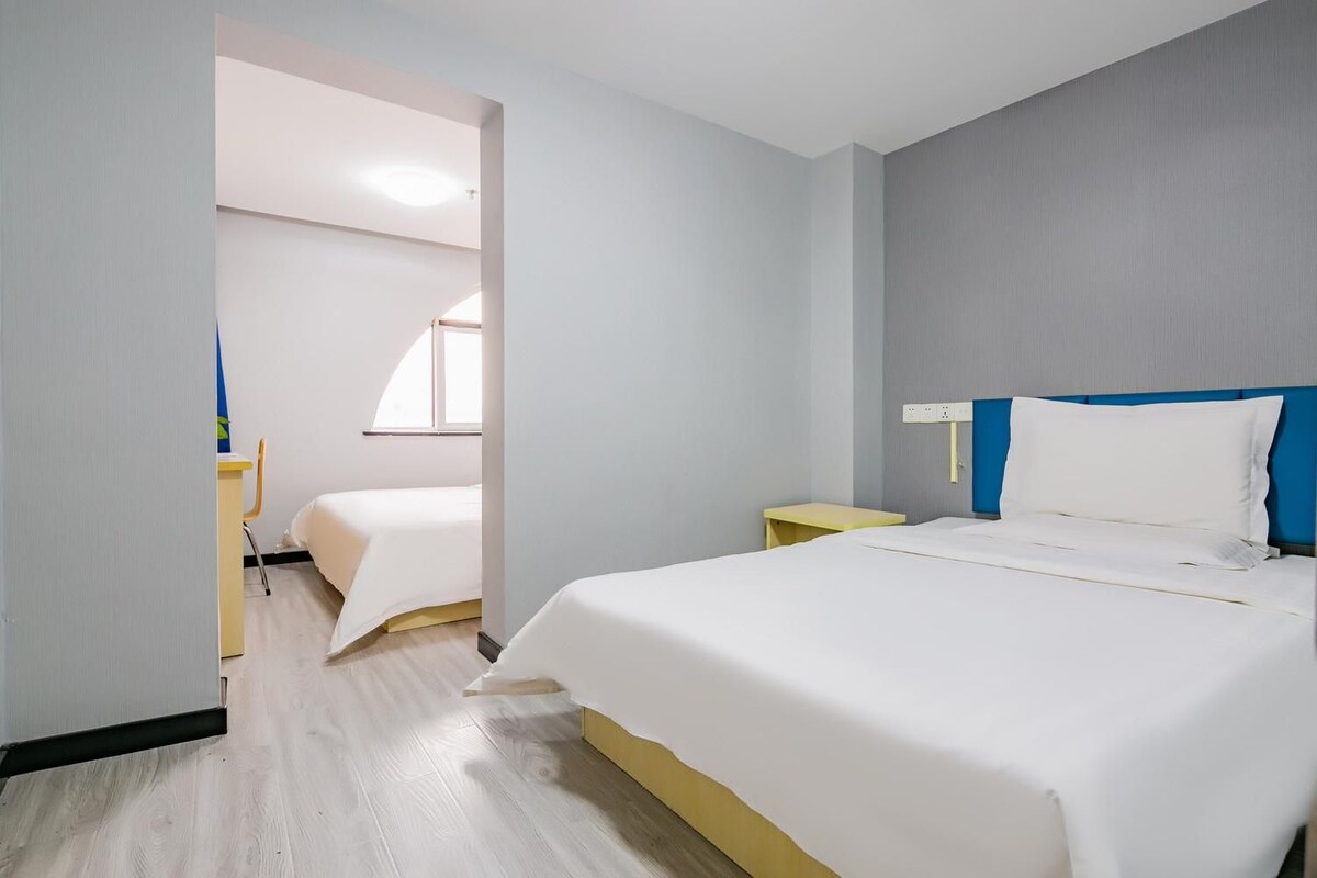 A hotel room with a large bed, a smaller bed, a desk, and a chair.