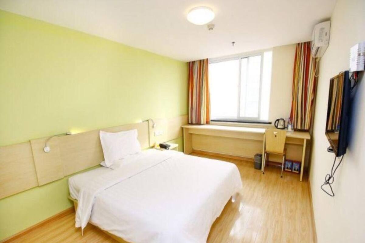 Una habitación de hotel con cama, escritorio, ventana con cortinas y televisor montado en la pared.