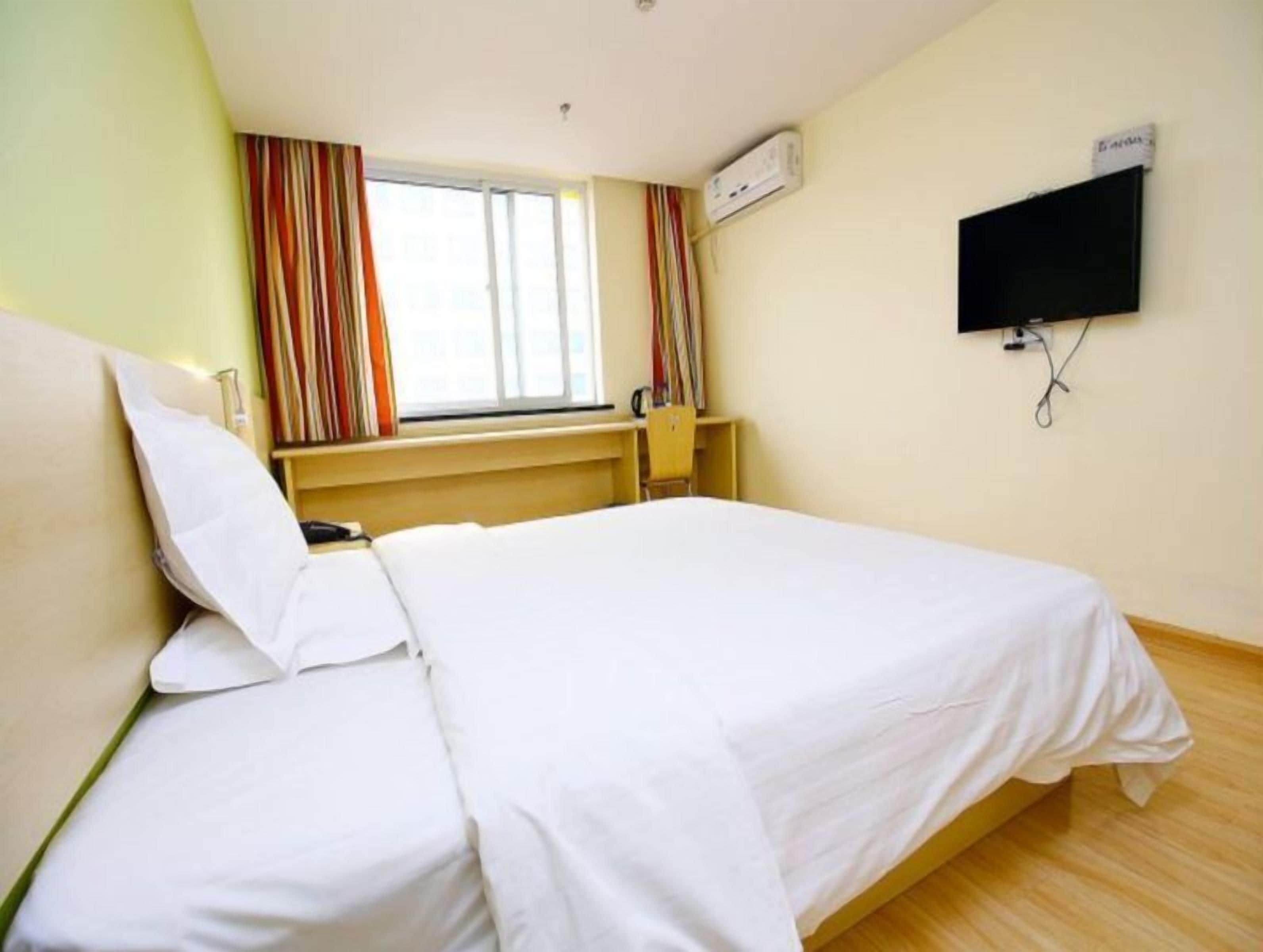 Quarto de hotel com cama, televisão fixada na parede e janela com cortinas.