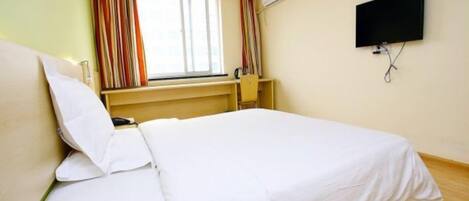 A hotel room with a bed, a television mounted on the wall, and a window with curtains.