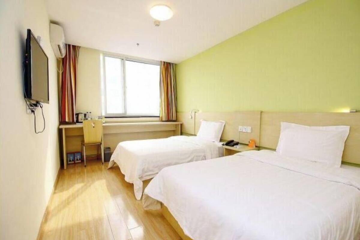 Habitación de hotel con dos camas, un escritorio, una silla, un televisor y una ventana con cortinas.