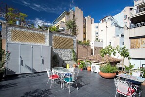 An outdoor patio area with metal chairs and tables, surrounded by potted plants and a stone wall. - Architect designed studio (EP7R). Green rooftop! (Athina)