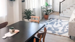 Un coin repas avec une table en bois foncé, deux chaises en bois, une plante en pot et un tableau encadré accroché au mur.