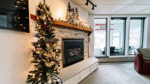 A living room with a fireplace, a Christmas tree, and a large window with a view of the outside. - 🔥 3 Min Walk to Lift | Center Village | Views + Parking (Frisco)