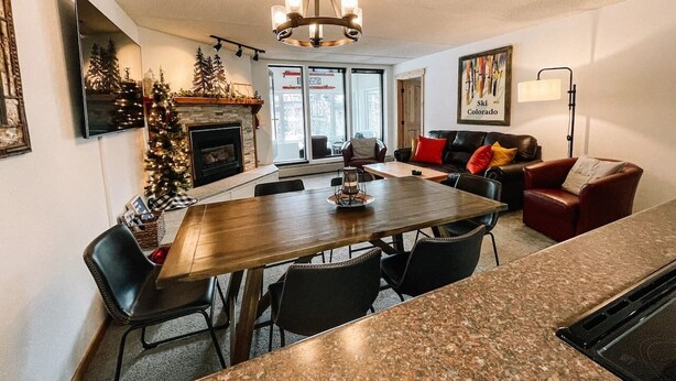 A modern kitchen with a dining area, a fireplace, and a living room with a couch and a coffee table. - 🔥 3 Min Walk to Lift | Center Village | Views + Parking (Frisco)