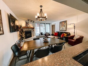 A modern kitchen with a dining area, a fireplace, and a living room with a couch and a coffee table. - 🔥 3 Min Walk to Lift | Center Village | Views + Parking (Frisco)