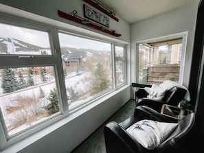 Enjoy a serene view of the surrounding landscape from the large window, accompanied by a comfortable black leather chair and a potted plant.