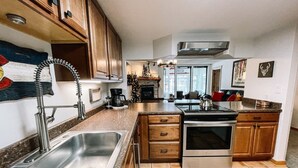 A kitchen with wooden cabinets, a stainless steel sink, a stove, and a tiled floor. - 🔥 3 Min Walk to Lift | Center Village | Views + Parking (Frisco)