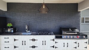A modern kitchen with a black brick backsplash, a stainless steel sink, a gas stove, and a built-in grill. - Palm's Bohemian House with Private Pool (Aguada)