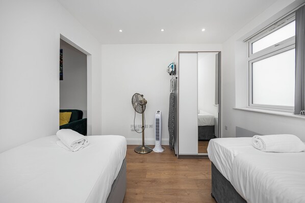 A modern hotel room with two beds, a standing heater, a mirror, and a window.