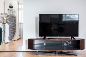 Ein modernes Wohnzimmer mit einem Flachbildfernseher auf einem Holzständer, einer Stehlampe und einer Wand mit Muster.