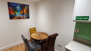 A dining area with a round table and chairs, a painting on the wall, and a 'First aid' sign. - Garland Stylish Apartment 2 In Greater London (Upper Belvedere, Kent)