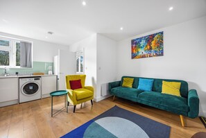 A modern living room with a green sofa, yellow armchair, and a colorful abstract painting.