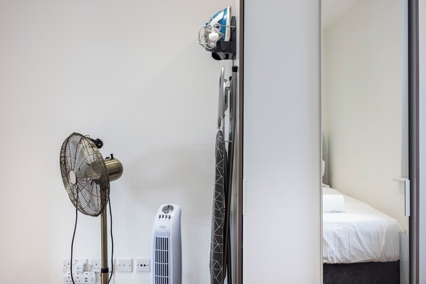 A room with a bed, a standing heater, and a wall-mounted fan.