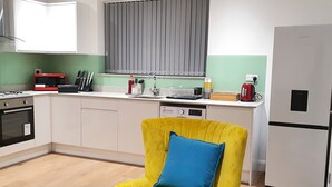 A modern kitchen with white cabinets, a yellow chair with a blue cushion, a red kettle, and a stainless steel refrigerator. - Garland Stylish Apartment 2 In Greater London (Upper Belvedere, Kent)