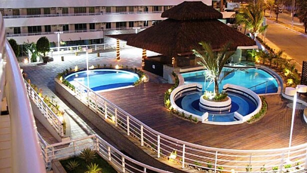 A hotel with multiple swimming pools, a central water feature, and a large thatched umbrella.