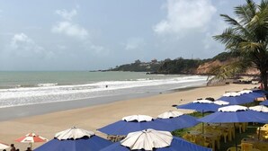 A beachside café with blue and white umbrellas, yellow chairs, and tables overlooking the ocean.