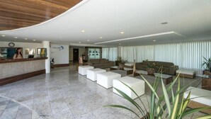 A modern lobby with a reception desk, seating area, and a large window with curtains.