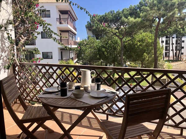 A balcony with a table set for dining, surrounded by wooden chairs and a lattice fence.