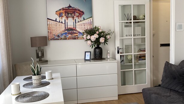 Una sala de estar moderna con comedor, una araña, un cuadro decorativo, un jarrón con flores y una estantería.