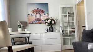 Una sala de estar moderna con alfombra gris, una silla de madera, un mueble blanco, un sofá gris, una araña y un cuadro de un pabellón.