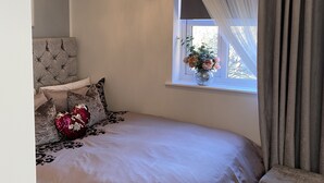Un dormitorio con una cama grande, un candelabro, una ventana con cortinas y un cabecero.