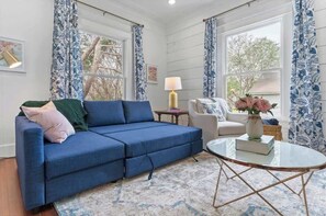 A room with a blue sofa, a white armchair, a small table with a vase, and patterned curtains. - Luxurious & Classic Southern Style, Sleeps 10 (Waco)