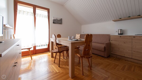 A cozy room with a wooden dining table, chairs, a sofa, and a kitchen area with wooden cabinets.