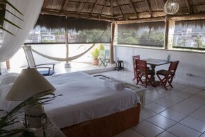 A hotel room with a bed, a small table, and chairs. There is a hammock and a potted plant.