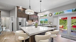 A modern kitchen with a large island, stainless steel appliances, and a view to the outdoors. - Coastal Escape: 2BR/2B w/King En-suite + Balcony Views, Deck, BBQ (Oceanside)