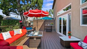 An outdoor patio with wicker furniture, a glass-top table, and a red umbrella. - Coastal Escape: 2BR/2B w/King En-suite + Balcony Views, Deck, BBQ (Oceanside)