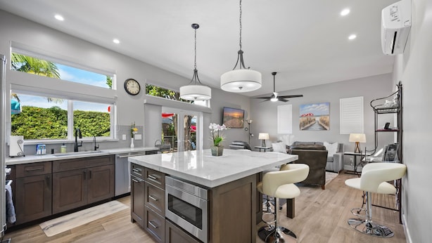 A modern kitchen with a large island, dark wood cabinets, stainless steel appliances, and a view of greenery outside. - Coastal Escape: 2BR/2B w/King En-suite + Balcony Views, Deck, BBQ (Oceanside)