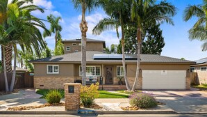 A two-story house with a stone facade, a garage, and a well-maintained lawn with palm trees. - Coastal Escape: 2BR/2B w/King En-suite + Balcony Views, Deck, BBQ (Oceanside)