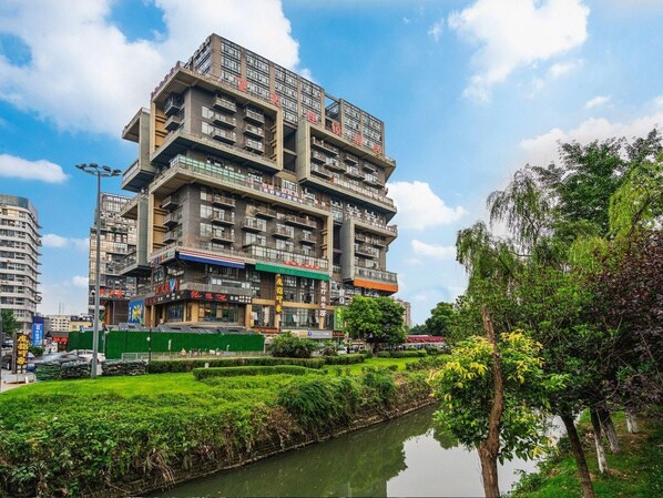A multi-story building with balconies, a river in front, and greenery.