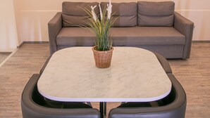 Ein modernes Zimmer mit einem runden Tisch, zwei Stühlen, einem grauen Sofa und einem Wandbild einer Landschaft.