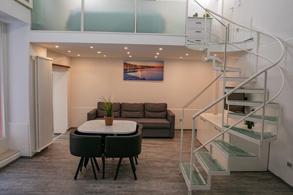 A modern interior with a dining area, a sofa, a staircase, and a cityscape painting.