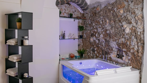 Ein modernes Badezimmer mit Steinwand, einer integrierten Badewanne und einem schwarzen Regalsystem.