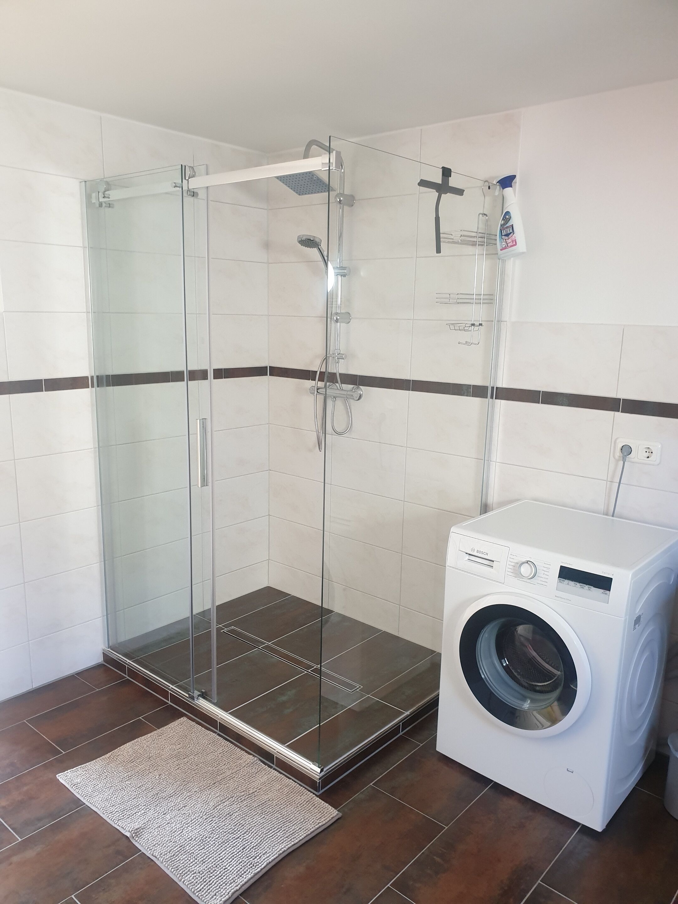 Une salle de bain moderne dotée d’une douche à parois de verre, d’un lave-linge Bosch et d’un sol carrelé.