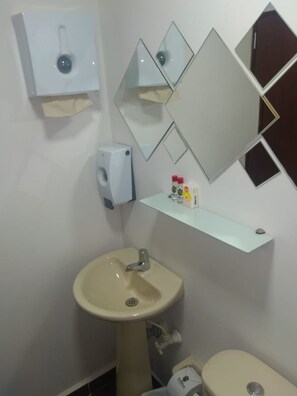 Een badkamer met een wastafel op een voetstuk, een toilet, een zeepdispenser en een spiegel met geometrische lijsten.