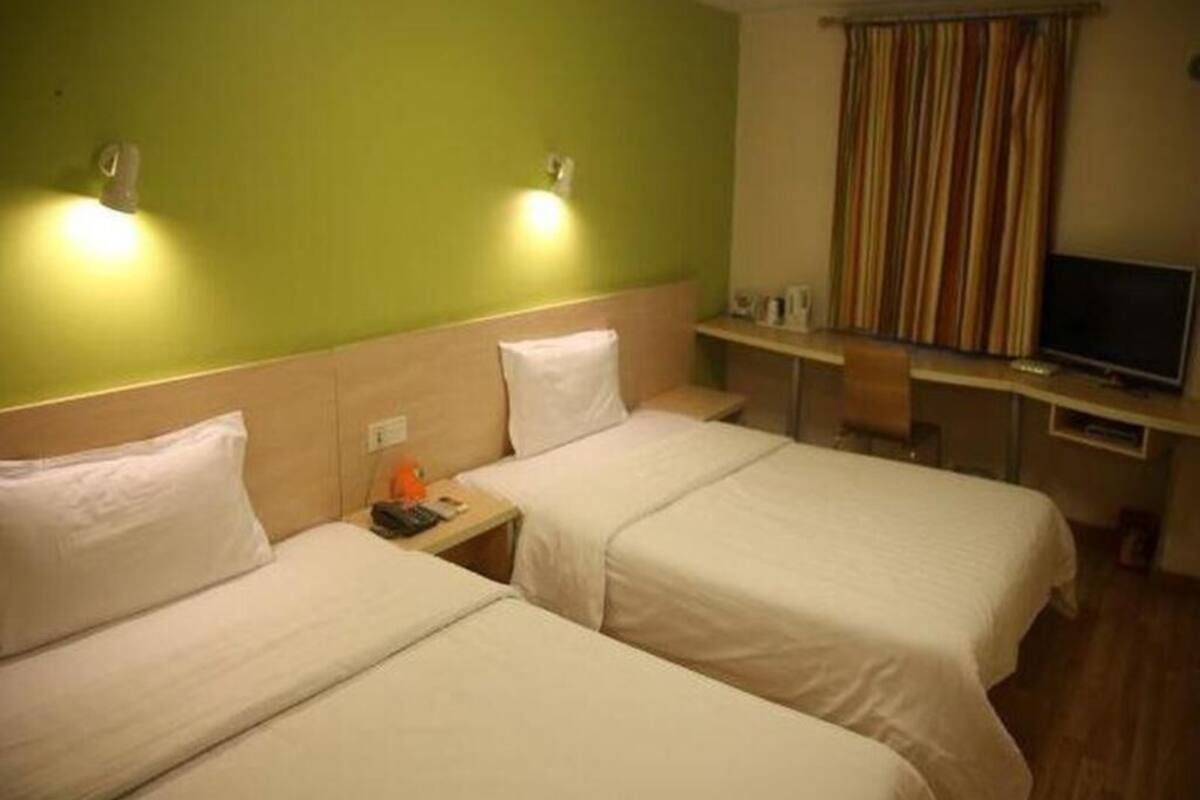 Hotellihuone, jossa on kaksi sänkyä, työpöytä, tuoli, televisio ja ikkuna, jossa on verhot.