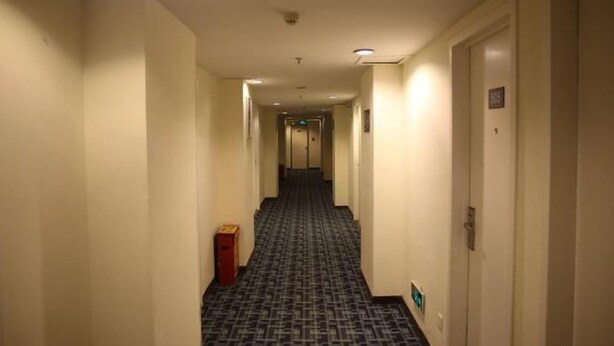 Un couloir d'hôtel avec des revêtements de sol en moquette, des portes de chaque côté et un détecteur d'incendie au plafond.