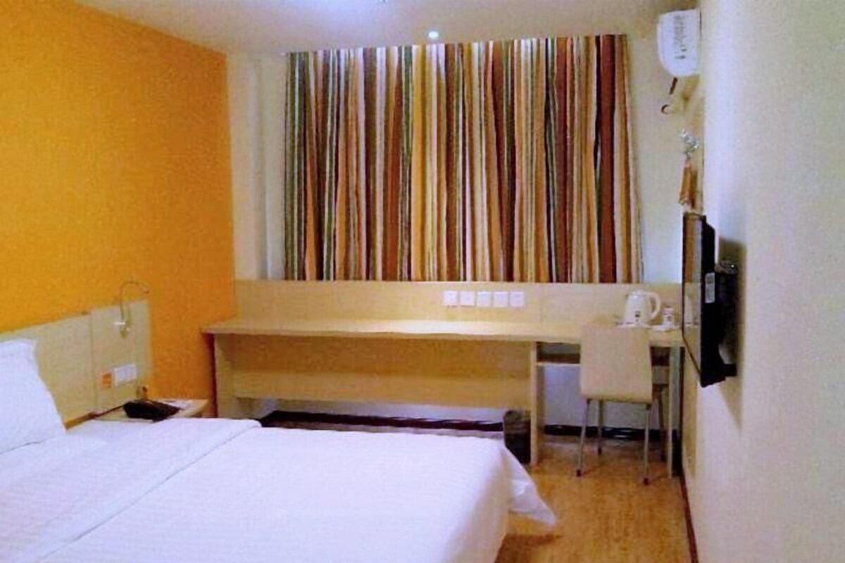 A hotel room with a bed, a desk, a chair, a television, and a striped curtain.
