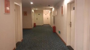 Un couloir d'hôtel avec des revêtements de sol en moquette, des portes de chaque côté et un luminaire au plafond.