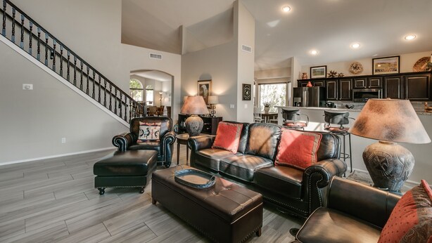 A spacious living room with a leather sofa, ottoman, and a staircase leading to another level. - Spectacular Golf Course Home with Pool and Views! (Gilbert)
