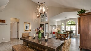 A spacious dining area with a wooden table, benches, and a chandelier. - Spectacular Golf Course Home with Pool and Views! (Gilbert)