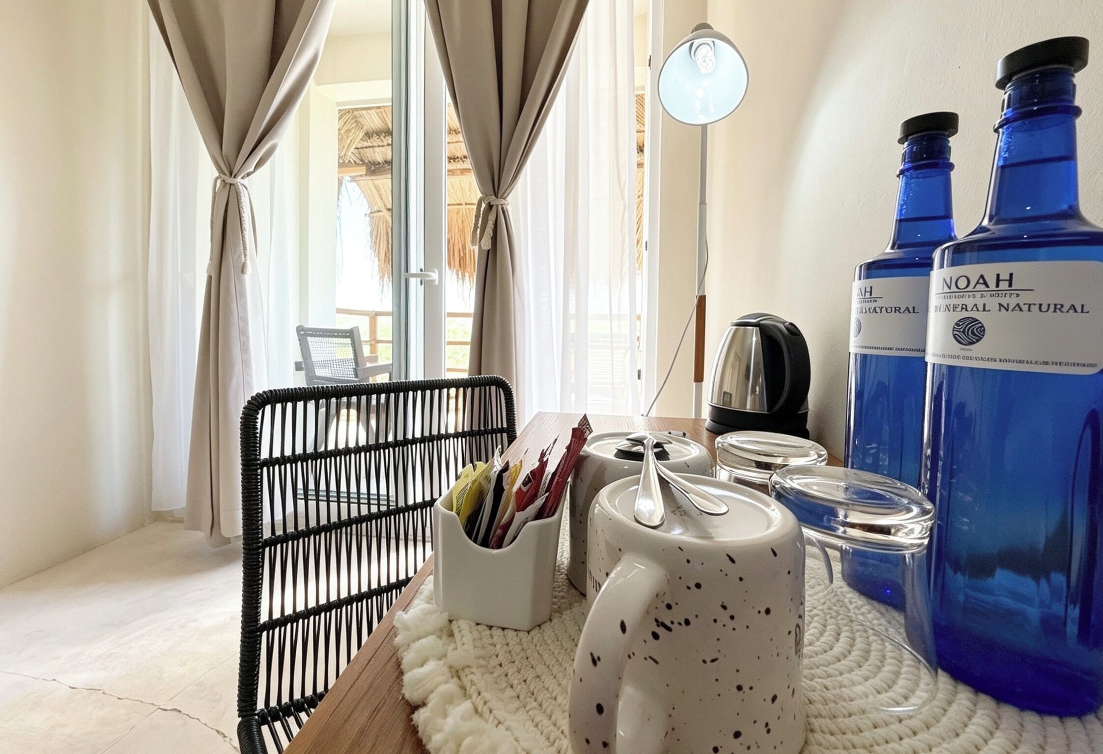 A room with a table set with a mug, a kettle, and a candle holder. There are two large blue bottles labeled 'NOAH' on the table.