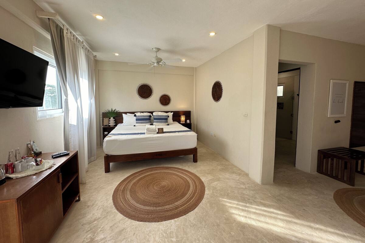 Ein Schlafzimmer mit einem Bett, einem Fernseher, einem Schreibtisch und einer Tür zu einem anderen Raum.